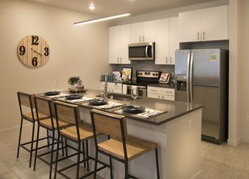 A kitchen with a large island with bar stools and a stainless steel refrigerator